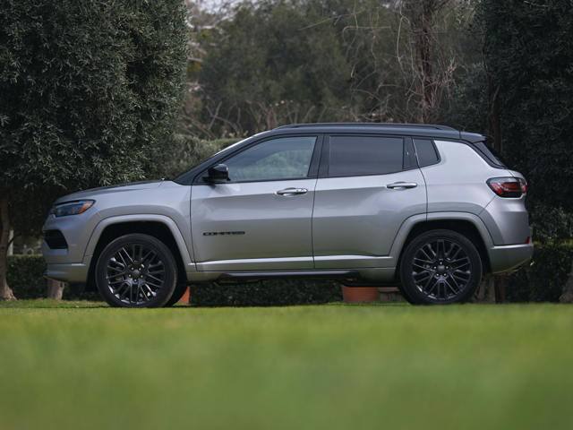 Profile view of a parked, silver 2024 Jeep Compass parked in the grass with trees in the background. | Auto service in Altoona, PA | Courtesy Motor Sales