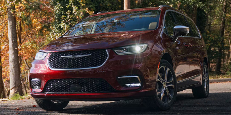 A red Chrysler Pacifica minivan parked on a road surrounded by autumn trees.