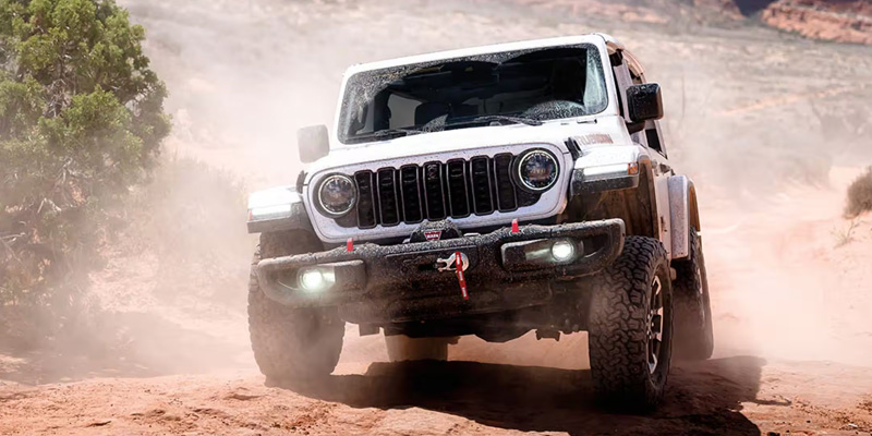 White Jeep Wrangler driving off-road through a dusty desert trail.